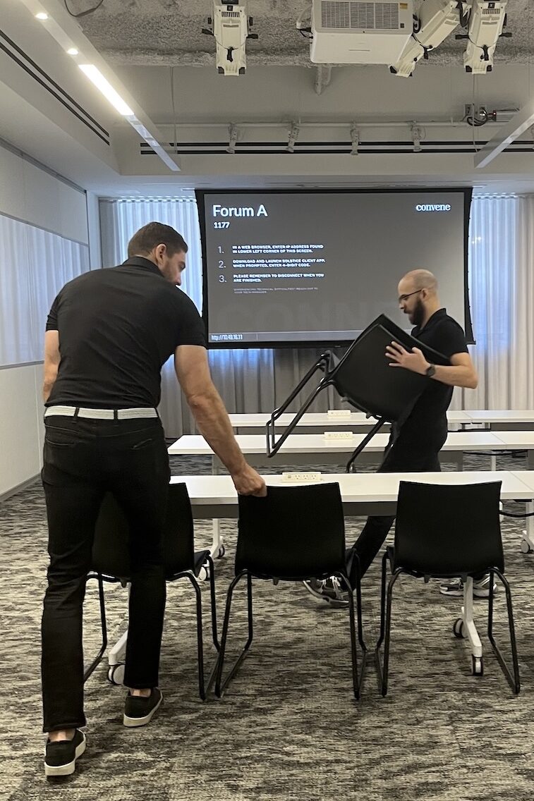Two people stacking chairs in a conference room at Convene in New York City.