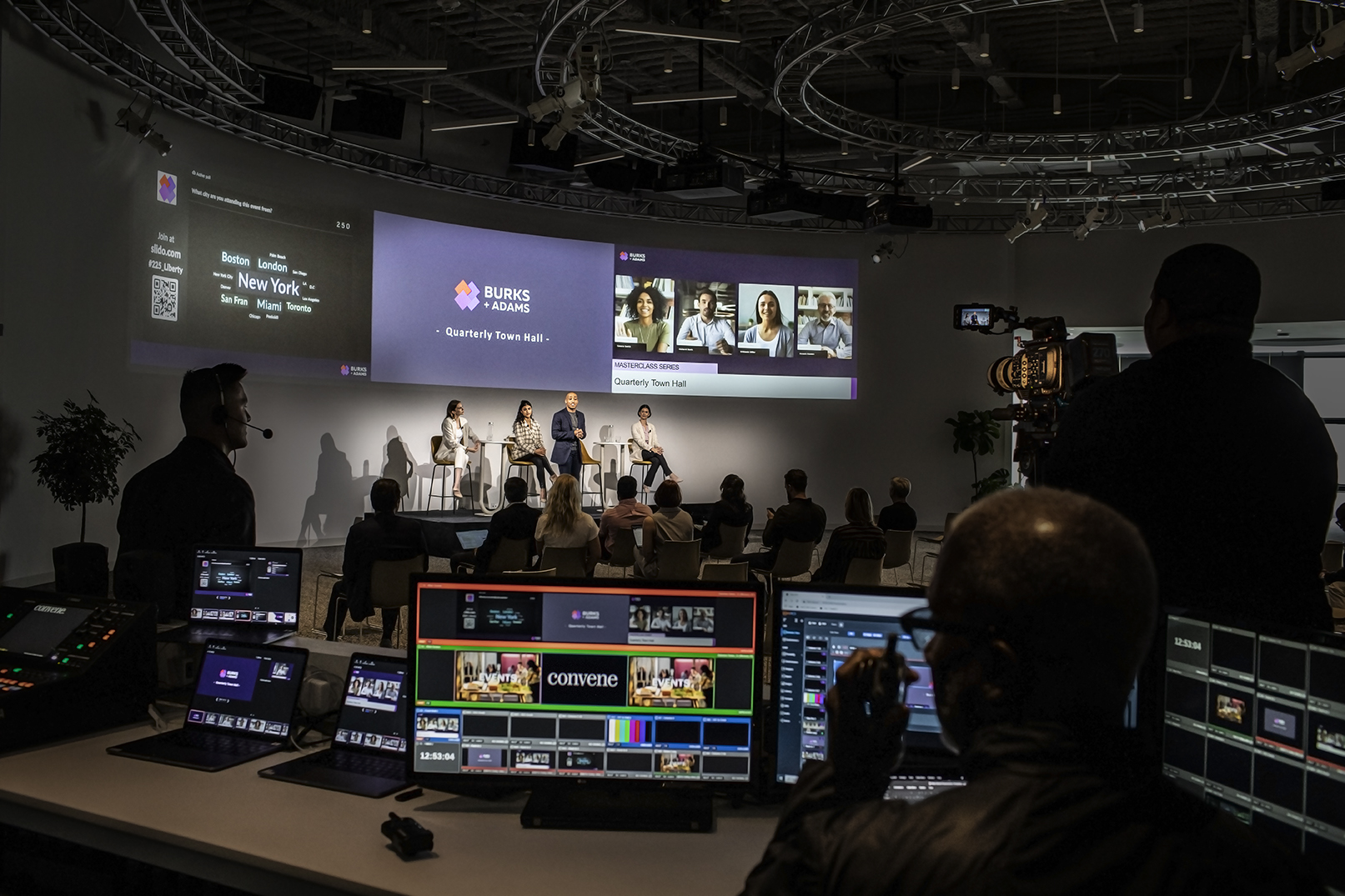 A large Convene meeting and event space. On stage there are a number of people who are presenting to a crowd.